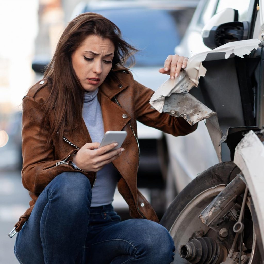 KFZ Gutachter Zentrale | young sad woman text messaging smart after car crash road KFZ Gutachter Zentrale