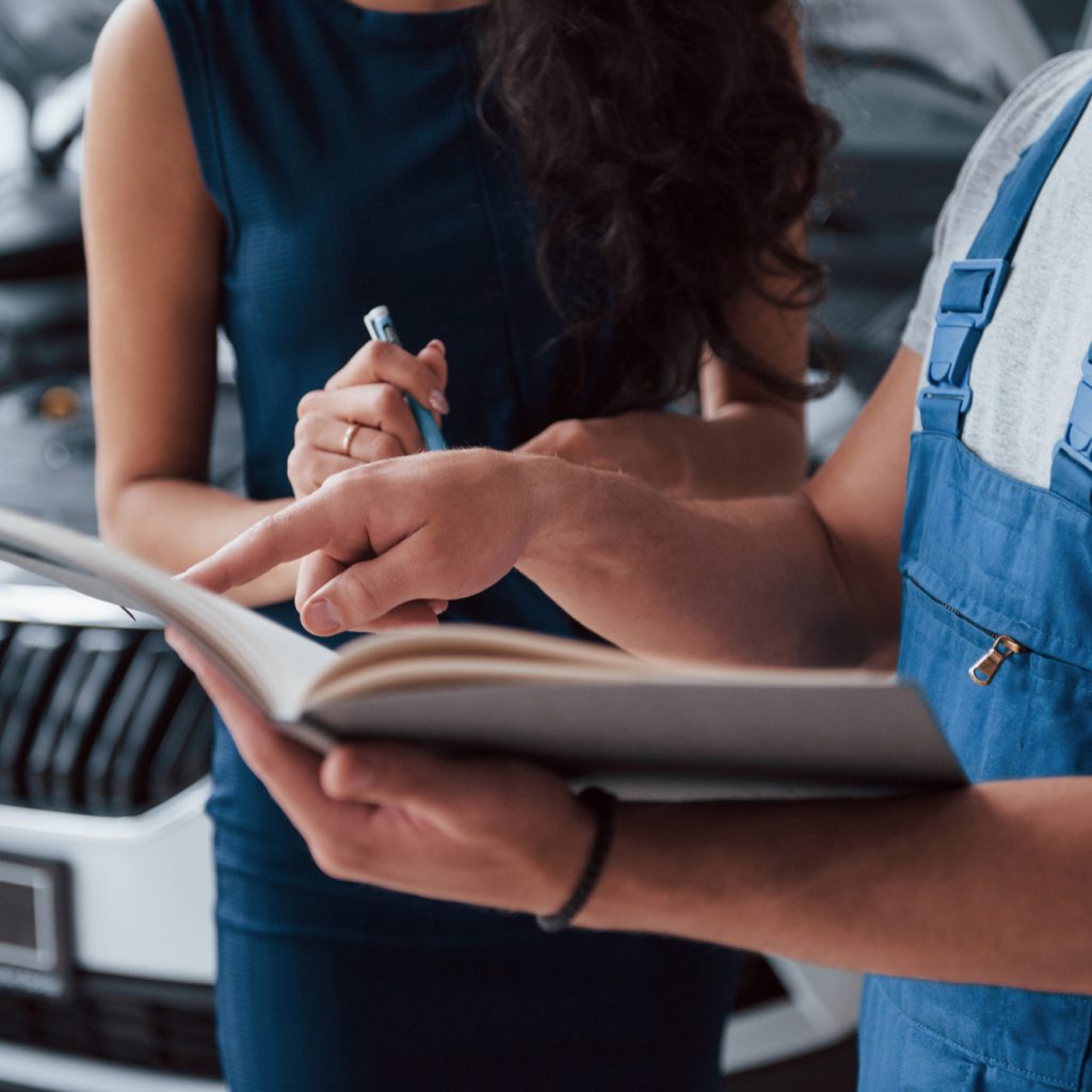 KFZ Gutachter Zentrale | your signature please woman auto salon with employee blue uniform taking her repaired car back KFZ Gutachter Zentrale